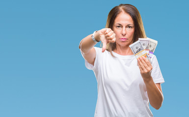 Middle age hispanic woman holding bunch of dollars over isolated background with angry face, negative sign showing dislike with thumbs down, rejection concept