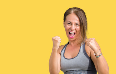 Beautiful middle age woman wearing sport clothes over isolated background very happy and excited doing winner gesture with arms raised, smiling and screaming for success. Celebration concept.