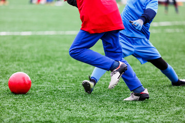 Young Active sport heathy boy in red and blue sportswear running and kicking a red ball on football field