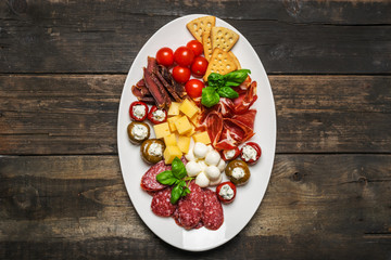 Various appetizers of cold meats, cheese, bacon, crispy crackers, olives on aged wooden background. Antipasto is a traditional Italian. Copy space. View from above. Flat layout.