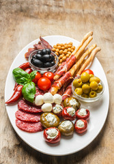 Various appetizers of cold meat, cheese, bacon, grissini bread sticks, olives on aged wooden background. Antipasto is a traditional Italian. Copy space. View from above. Flat layout.
