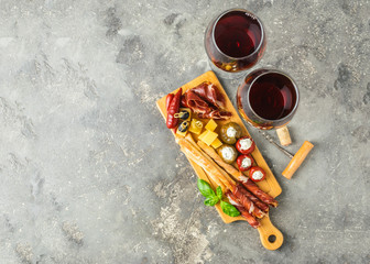 Cold appetizer, smoked meat, bread sticks of grissini, pepper, olives and two glasses of red wine on a gray background. Tapas bar. Antipasto View from above. Flat layout. Copy space.