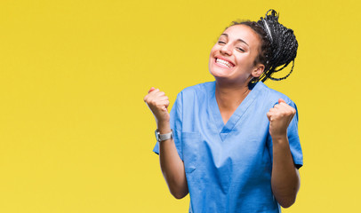 Young braided hair african american girl professional nurse over isolated background celebrating surprised and amazed for success with arms raised and open eyes. Winner concept. - obrazy, fototapety, plakaty