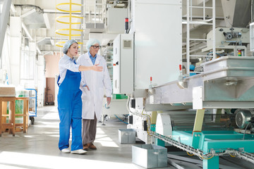 Full length portrait of young female worker showing machine units in factory to senior woman, copy space - Powered by Adobe