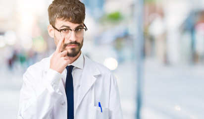 Young professional scientist man wearing white coat over isolated background Pointing to the eye watching you gesture, suspicious expression