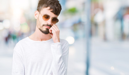 Young handsome man wearing sunglasses over isolated background thinking looking tired and bored with depression problems with crossed arms.