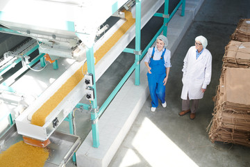 High angle portrait of two smiling factory workers walking down hall in modern food production workshop, copy space