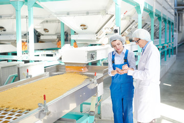 Portrait of two women working at factory  standing by conveyor belt at modern  food production,...