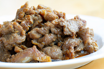 Stir fry pork slice with coconut sugar sprinkle with fried shallot slice (Sweet pork) in white dish on wooden table, delicious Thai food