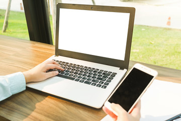 Close-up of Business woman working with smartphone,laptop with blank white screen and document in coffee shop like the background.