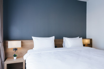 Close-up of white pillow on bed decoration with light lamp in hotel bedroom interior.