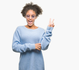 Young afro american woman wearing glasses over isolated background smiling with happy face winking at the camera doing victory sign. Number two.