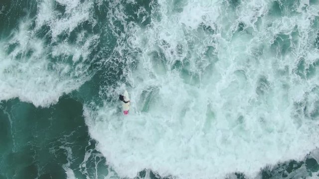 Areal footage above sea showing a surfer trying to make his way to the deeper water through the waves crashing at him and his surfboard. 4k video quality