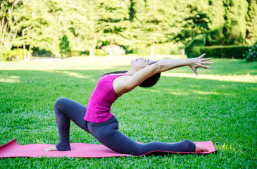 Woman imaking asana mermaid pose. Variation of rajakapotasana. Healthy lifestyle in the park. Stretching.