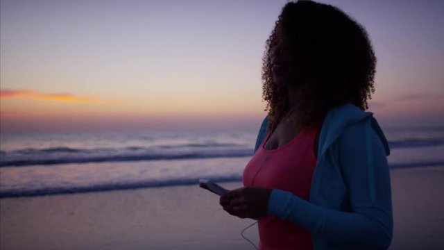 Attractive afro hair Ethnic African American female doing light exercise on the beach walking carefree with music and ear buds  