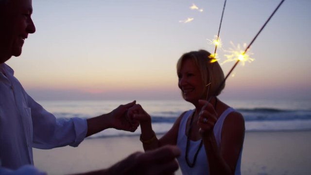 Caucasian seniors enjoying beach party with sparklers at sunset - Powered by Adobe