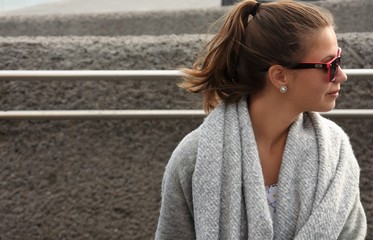 girl in a gray scarf and in sunglasses sits looking to the side