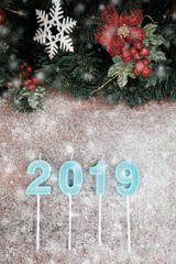 Year 2019 in blue color on wooden board and blurry showflake, border design with pine branches,...