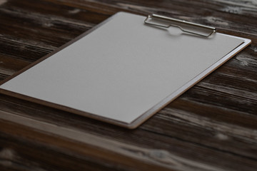 Clipboard with white sheet on wood background. Top view.Vintage style.