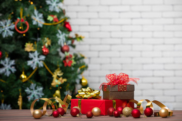Fototapeta na wymiar Classic red and golden gift boxes decorate with glitter balls, soft blurred background of Christmas tree and white brick wall for copy space at top area