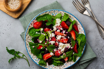 Beets, strawberries, feta cheese and arugula salad in ceramic plate on old concrete table background. Top view.