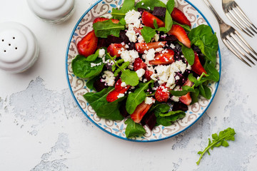 Beets, strawberries, feta cheese and arugula salad in ceramic plate on old concrete table background. Top view.