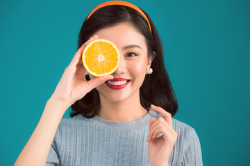 Healthy food. Smiling lovely pinup asian girl holding orange over blue background.
