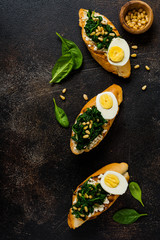 Fried spinach, egg and pine nuts sandwiches on brown vintage old concretebackground. Delicious healthy breakfast or snack. Top view.