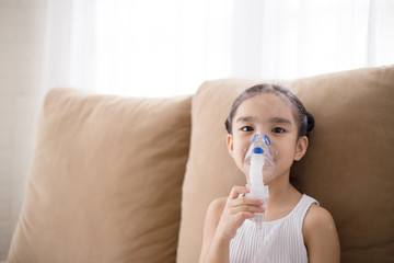 Cute Asian child patient inhalation therapy by the mask of inhaler with soft stream smoke from...