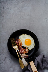 Traditional English breakfast with fried eggs and bacon in cast iron pan on old gray concrete background. Top view.