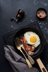 Traditional English breakfast with fried eggs and bacon in cast iron pan on dark concrete background. Top view.