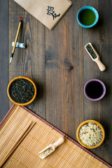 Chinese traditional symbols concept. Tea, rice, hieroglyph symbol, bambootabe mat, chopsticks, soy sause on dark wooden background top view frame space for text