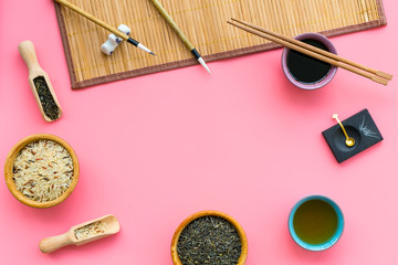 Fototapeta na wymiar Chinese traditional symbols concept. Tea, rice, hieroglyph symbol, bambootabe mat, chopsticks, soy sause on pink background top view frame space for text
