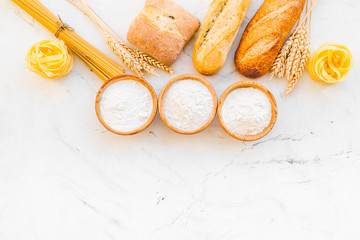 Homemade fresh bread and pasta near flour in bowl and wheat ears on white stone background top view copy space
