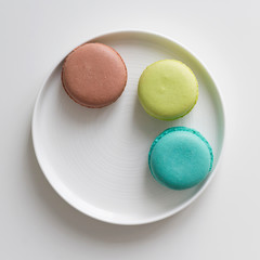 Turquoise, brown and green macarons in the white plate on the table. Top view, flat lay, copy space
