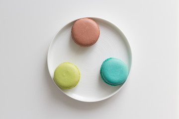 Turquoise, brown and green macarons in the white plate on the table. Top view, flat lay, copy space