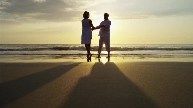 Silhouette of mature Caucasian couple dancing on the ocean beach at sunrise