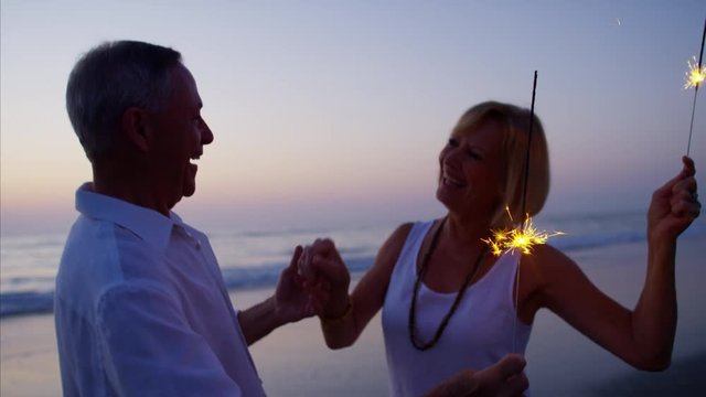 Mature Caucasian couple enjoying beach party with sparklers at sunset