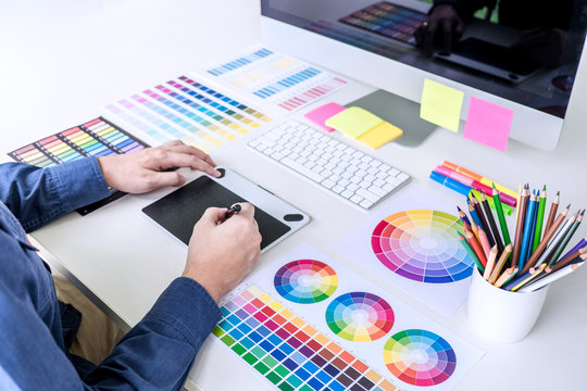 Male creative graphic designer working on color selection and color swatches, drawing on graphics tablet at workplace with work tools and accessories