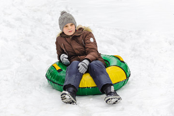 Fototapeta na wymiar Teen boy sitting on a tubing in the snow, resting