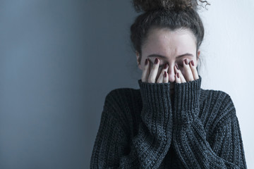 Close up of teenager with depression and bulimia sitting alone in dark room. She covers her face with hands. Mental problems with depression and bulimia. - obrazy, fototapety, plakaty