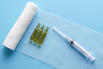 Tree brown ampoules and a sytinge. Ampoules on  a bandage. Sterile bandage on blue. Medical equipment on blue