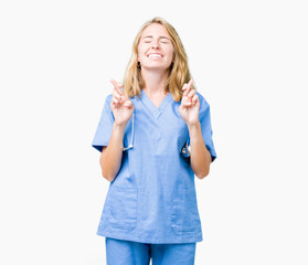 Beautiful young doctor woman wearing medical uniform over isolated background smiling crossing fingers with hope and eyes closed. Luck and superstitious concept.