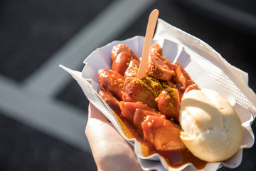 Frau  isst Currywurst unterwegs draußen am Wochenmarkt Imbiss