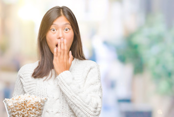 Young asian woman eating popcorn over isolated background cover mouth with hand shocked with shame for mistake, expression of fear, scared in silence, secret concept