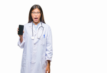 Young asian doctor woman holding smartphone over isolated background scared in shock with a surprise face, afraid and excited with fear expression
