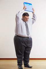 Frustrated obese man wearing formal clothes lifting a weighing scale over his head to throw it