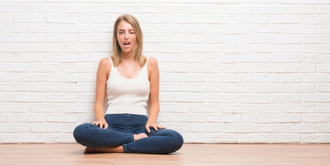 Beautiful young woman sitting on the floor at home winking looking at the camera with sexy expression, cheerful and happy face.