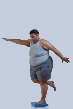Obese man balancing on weighing scale with one leg with his hands spread across