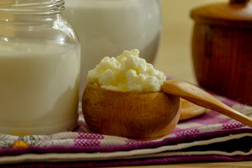 Homemade milk kefir and kefir grain - oraganic probiotic drink. Wooden spoon and bowl, and glass jar and ewer on kitchen table.